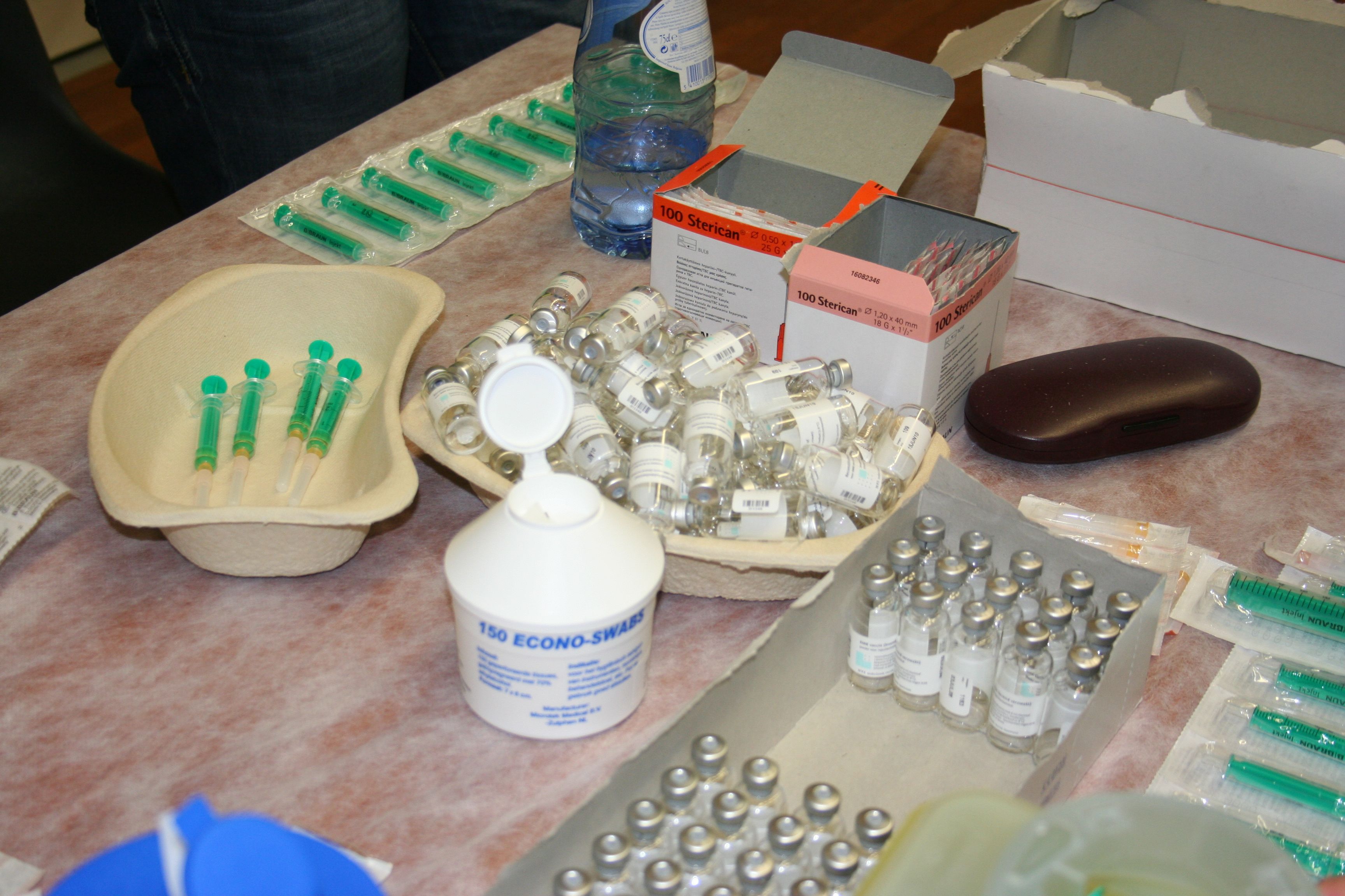 Afbeelding van een kartonnen nierbekken met injectienaalden. Kartonnen nierbekken en doos met ampullen en een pot met alcoholdoekjes.