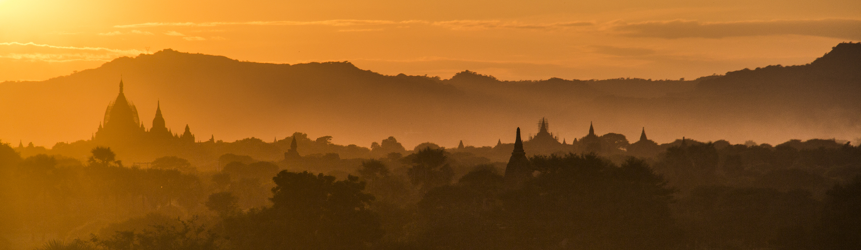Afbeelding van oranje kleurige stad in Myanmar door de zonsopkomst. Op de achtergrond bergen. 