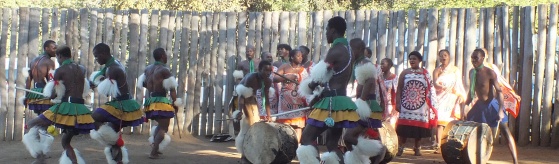 Foto van een groep mensen in Zuid-Afrika in dezelfde kleding. Ze maken muziek en dansen.