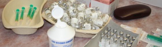 Afbeelding van een kartonnen nierbekken met injectienaalden. Kartonnen nierbekken en doos met ampullen en een pot met alcoholdoekjes.