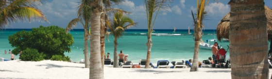 Wit palmenstrand met helderblauwe zee. Op het strand staan ligbedden.
