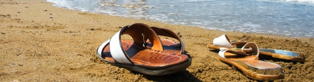 Twee paar slippers op het strand net voor de branding van de zee.