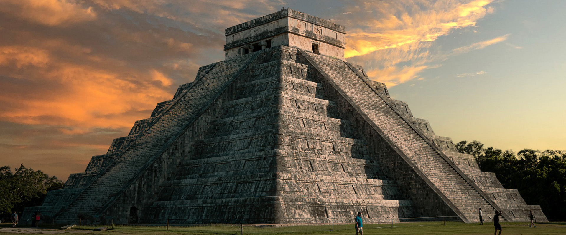 Header afbeelding van van Maya tempel in Mexico. Voor de tempel lopen een paar mensen en op de achtergrond de zonsondergang met oranje kleurige lucht. 